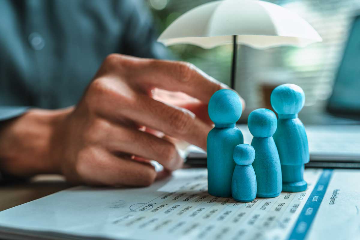 Wooden family figures under an umbrella symbolizing employee benefits planning and health insurance protection